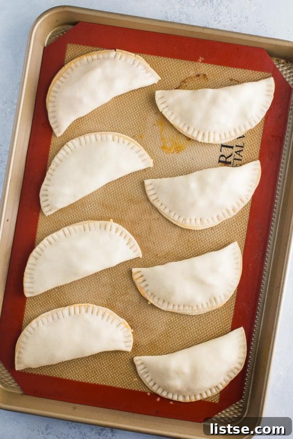 stack of six baked chicken empanadas on a wire rack, with a bowl of salsa in the background