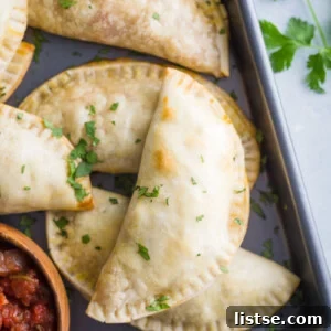 empanadas stacked up on a back tray with salsa in the corner
