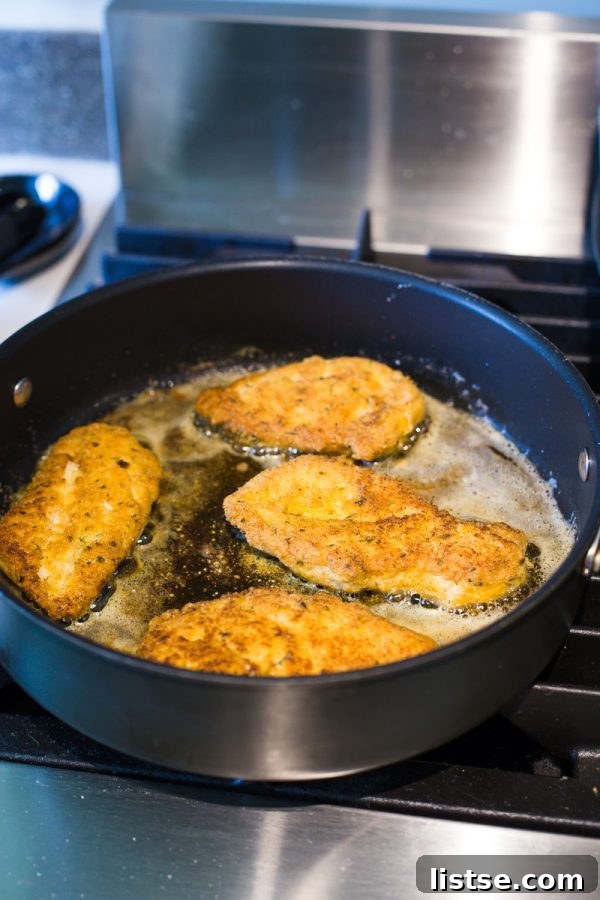 Pan-frying keto-breaded chicken breasts to a golden brown before baking.
