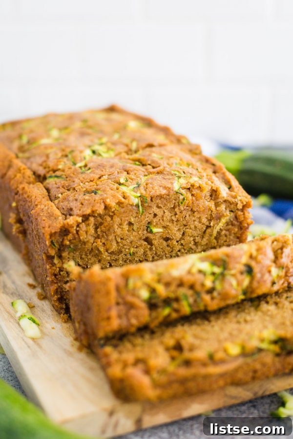 Moist Vegan Zucchini Loaf 7 A beautiful side view of a freshly baked loaf of vegan zucchini bread, sliced and artfully arranged on a wooden board. The setting is enhanced with a cozy blue checkered towel and a fresh zucchini in the background, inviting viewers to savor this wholesome, homemade treat.