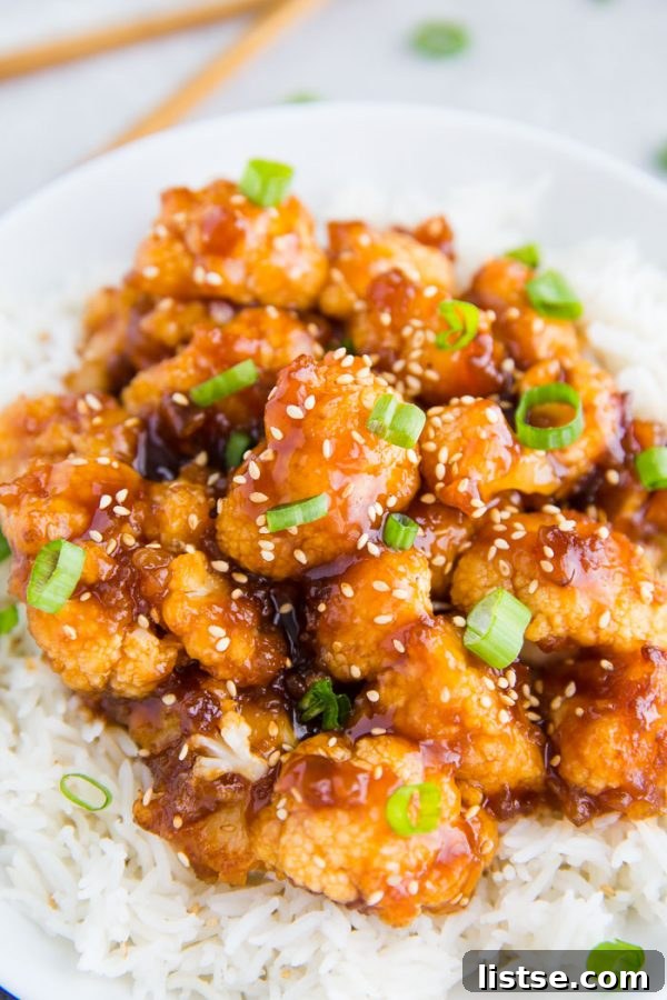 A bowl of Sweet and Sour Cauliflower garnished with sesame seeds and green onions, served with fluffy white rice.