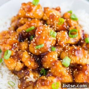 Sweet and Sour Cauliflower, garnished with sesame seeds and green onions, served as a plant-based main course.