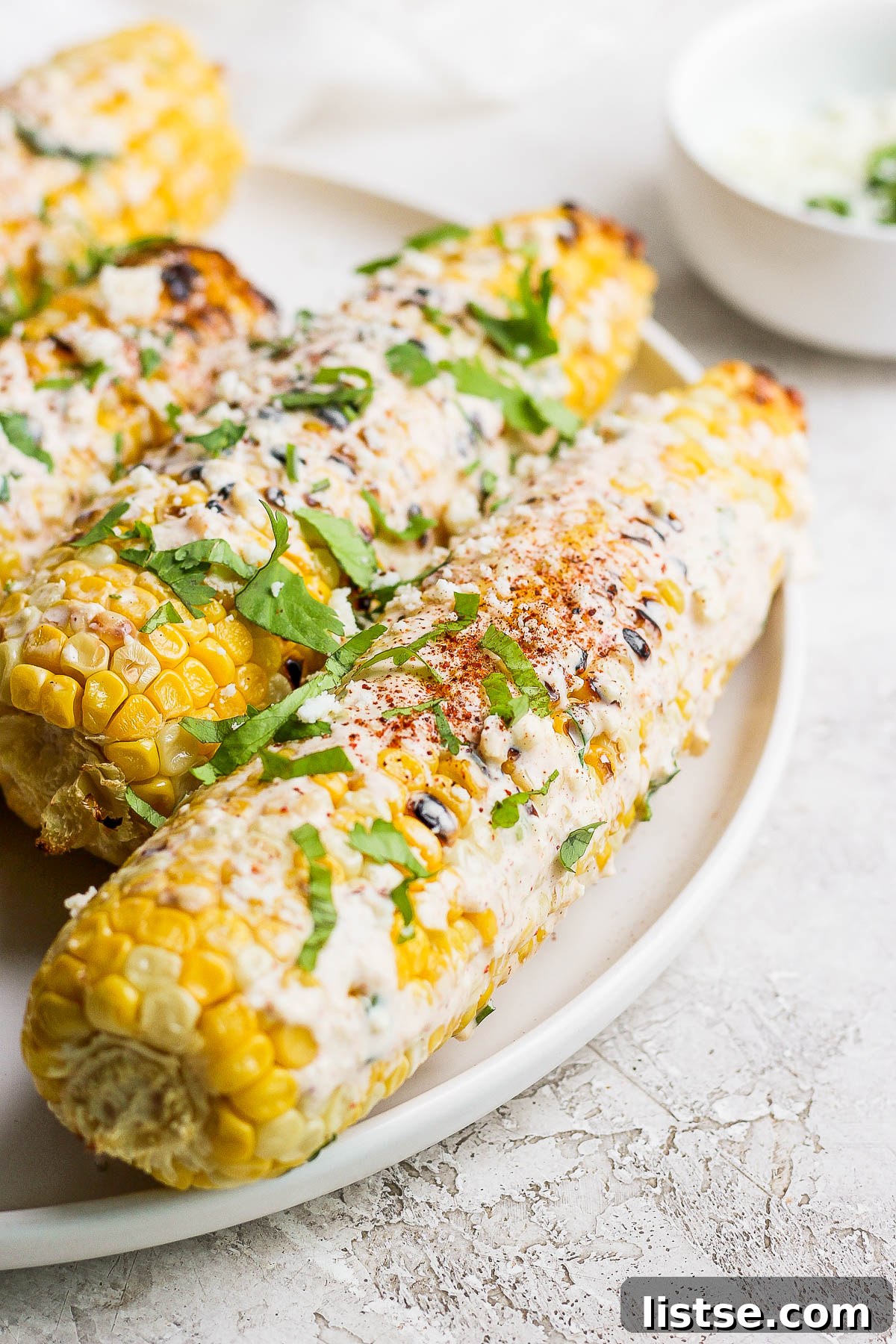 Grilled Mexican street corn on the cob, garnished with cilantro and Cotija cheese, served on a white plate.