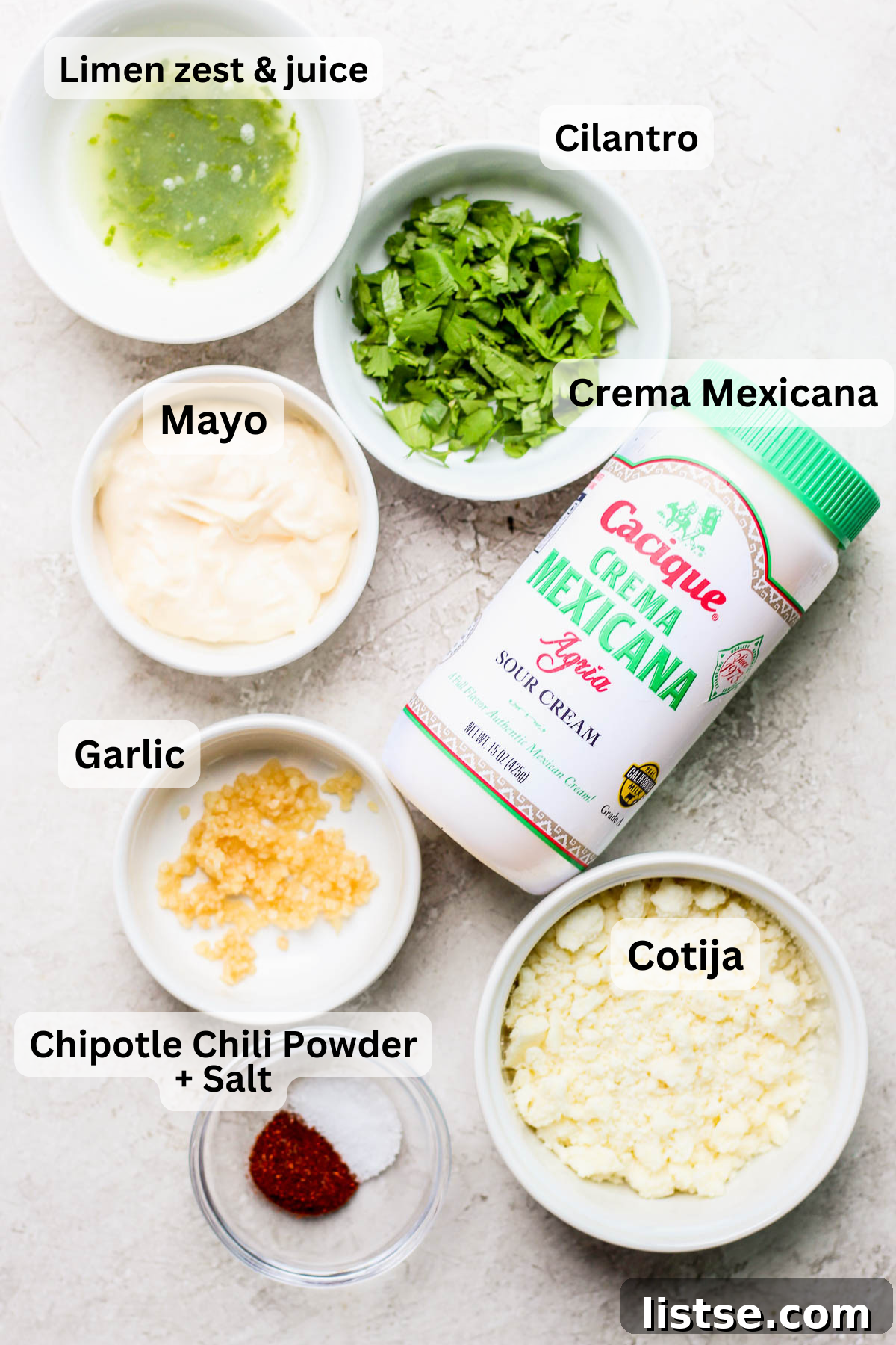 Arrangement of fresh ingredients for Mexican street corn sauce, including corn, crema, mayonnaise, cheese, and lime.