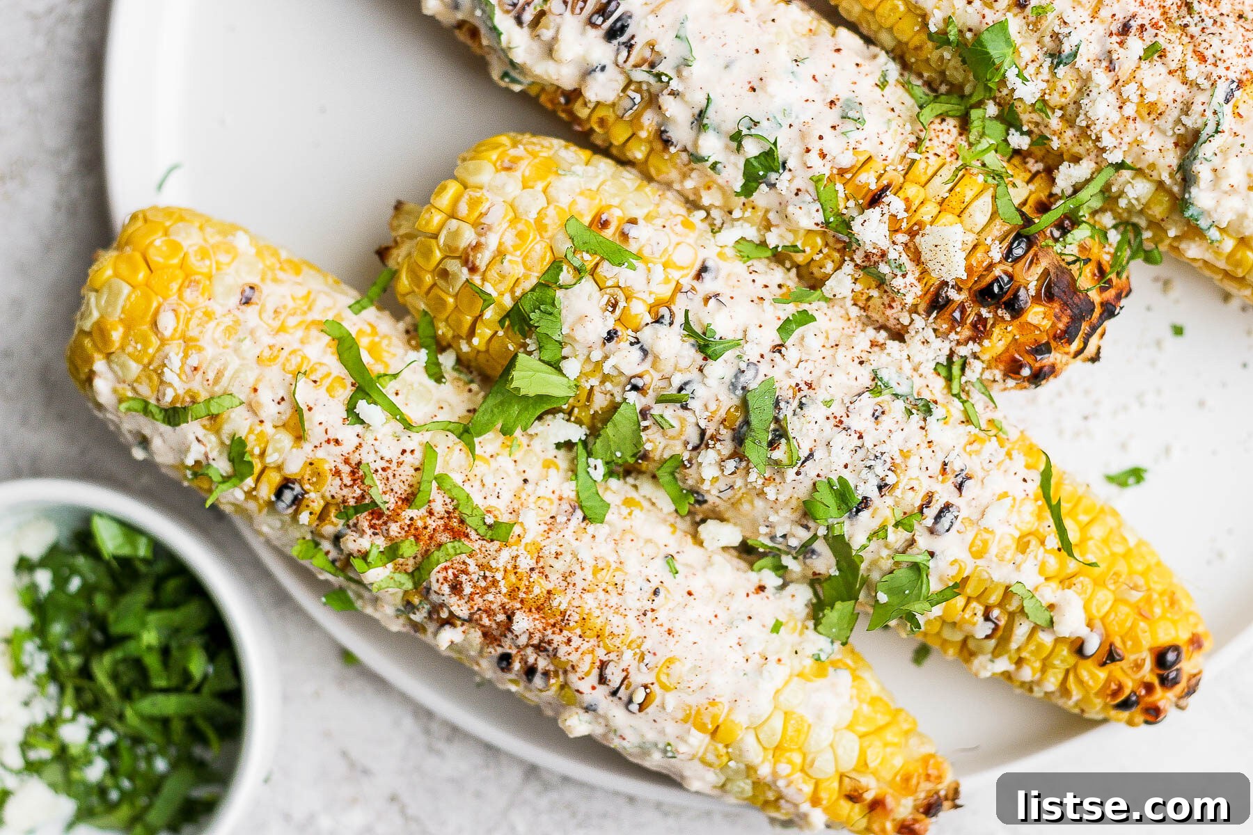 Fully dressed Mexican street corn on a white plate, garnished with cilantro and extra Cotija cheese.