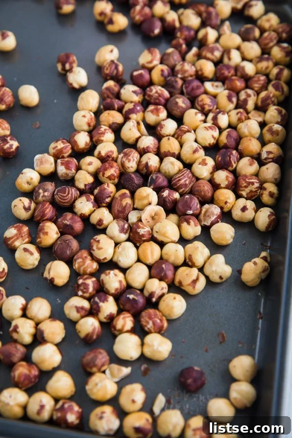 Roasted hazelnuts spread on a baking sheet, ready for skin removal, showcasing their warm, inviting color.