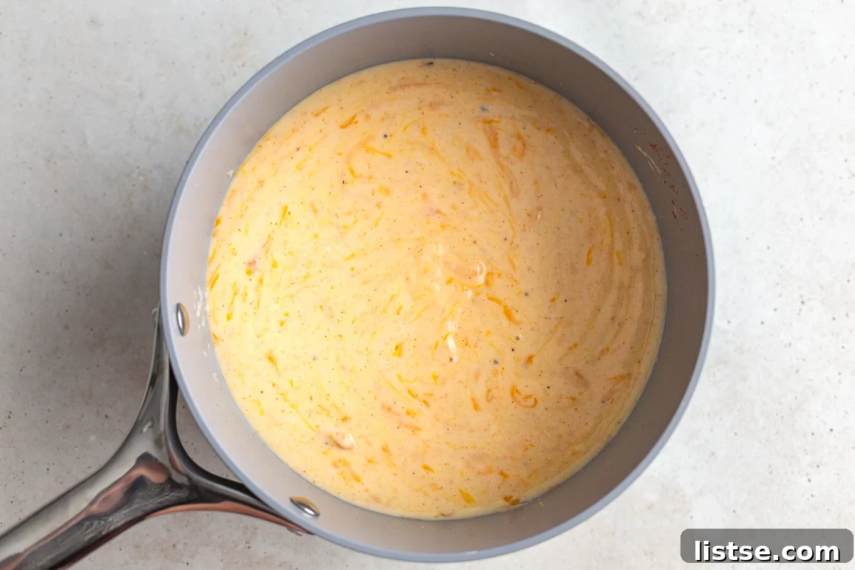 Shredded cheddar cheese being stirred into the creamy sauce