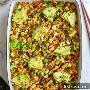 Vegetarian sushi bake inside of a casserole dish that's topped with heaps of avocado, sesame seeds and drizzled with red sriracha, orange spicy mayo, and kewpie mayo. It's also sprinkled with chopped green onion.