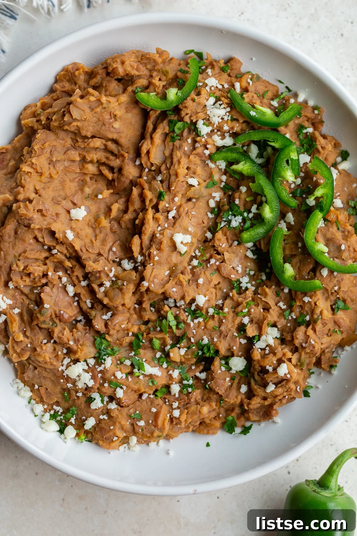 A large, rustic white bowl filled to the brim with creamy, perfectly mashed homemade refried beans, ready for serving