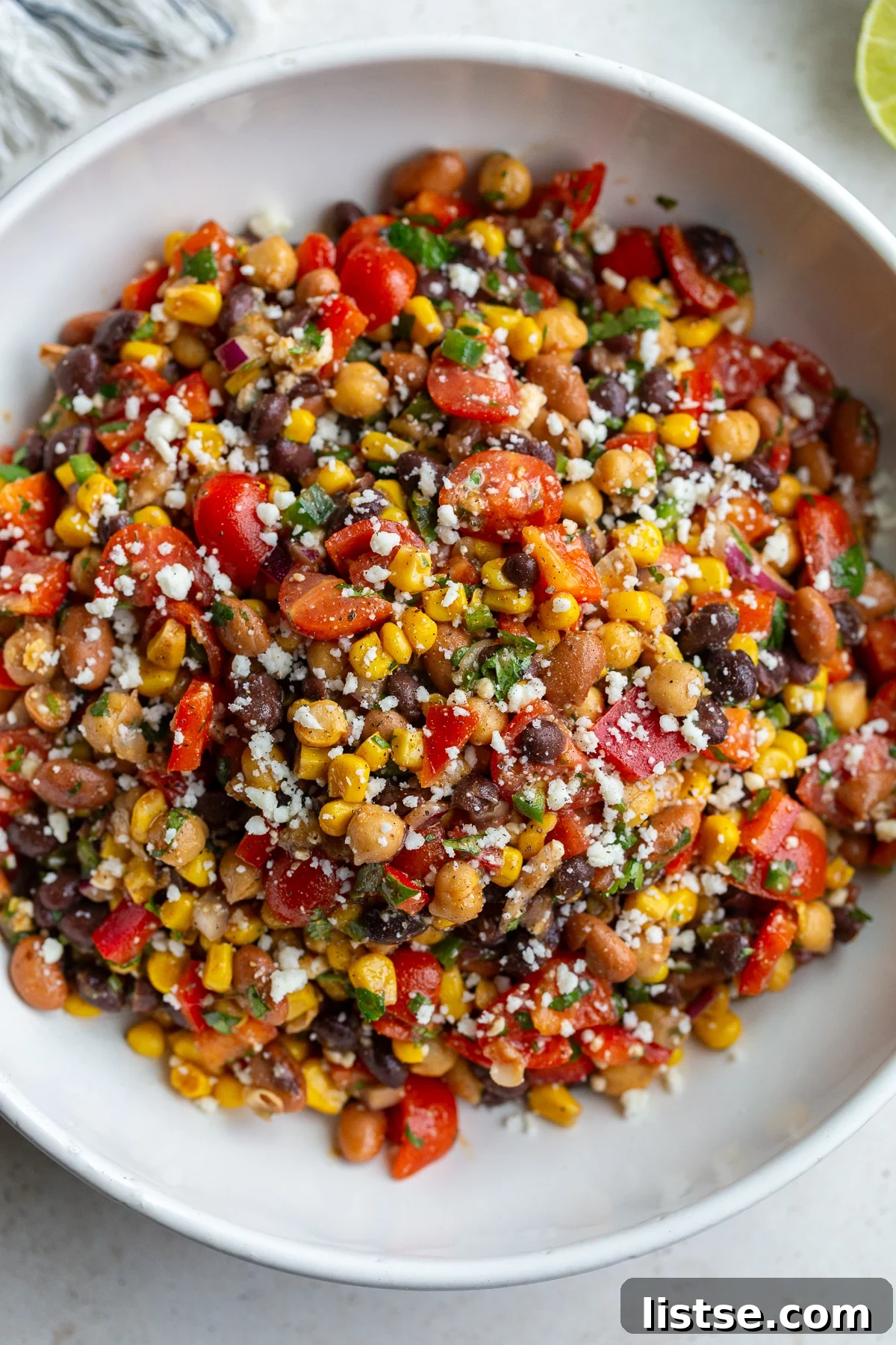Large bowl of Southwest bean salad filled with 3 types of beans and lots of veggies, with a spoon for serving