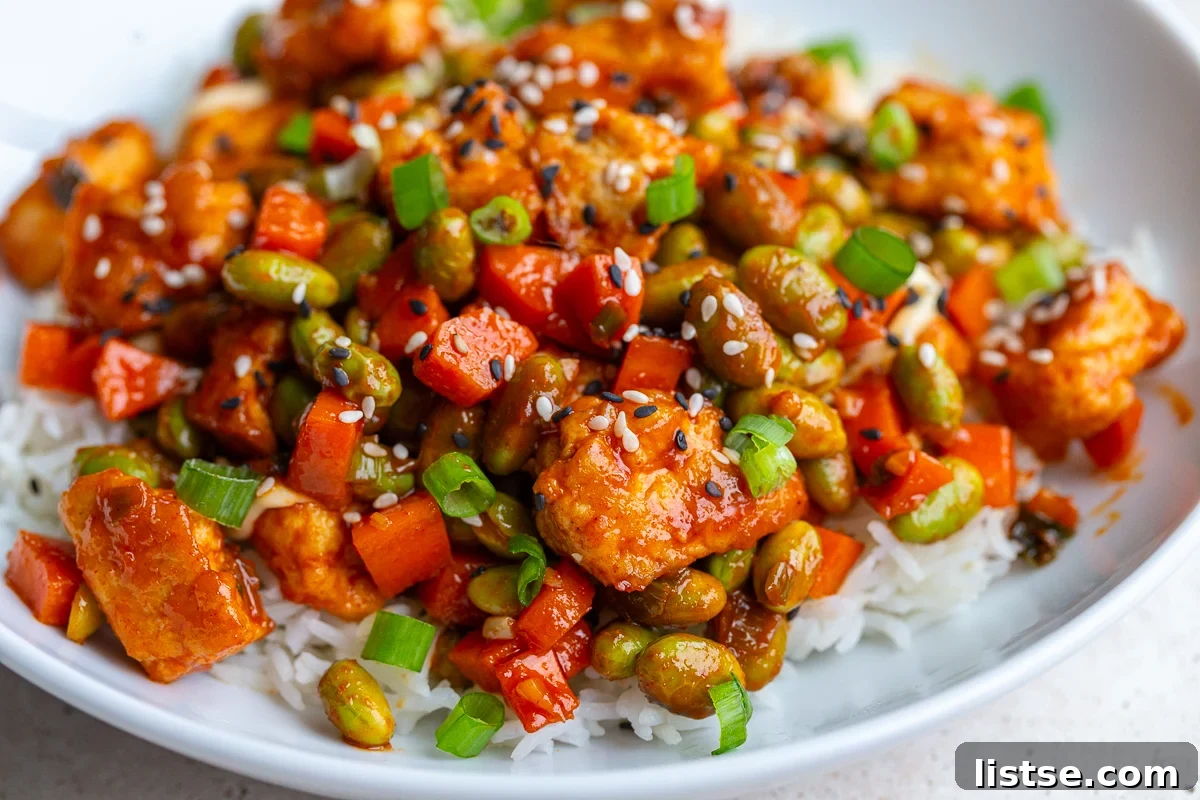 gochujang tofu and edamame stir fry in a large white bowl topped with sesame seeds