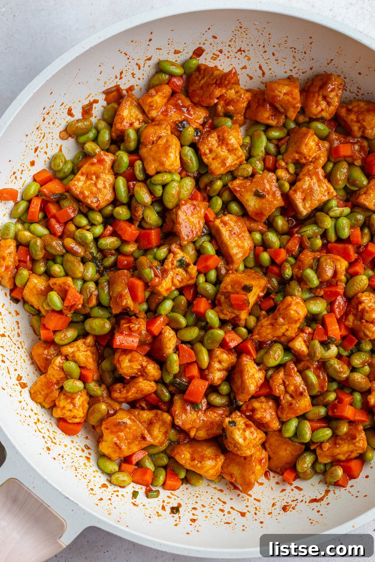 gochujang tofu and edamame stir fry in a large white skillet topped with sesame seeds