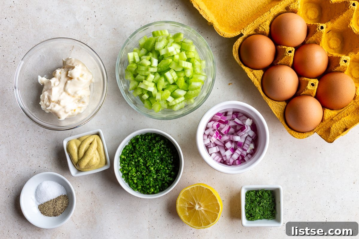 A vibrant flat lay showcasing all the fresh ingredients needed to make homemade egg salad sandwiches: hard-boiled eggs, creamy mayonnaise, fresh chives, diced red onion, crisp celery, and other essential seasonings, laid out on a wooden surface.