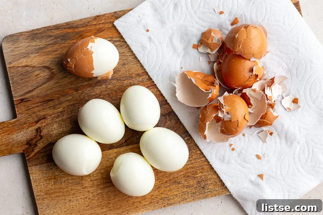 Two hard-boiled eggs, partially peeled, rest on a wooden cutting board, ready for the next step in preparing a delicious egg salad.