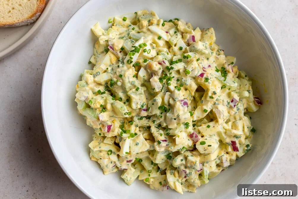 A large, inviting bowl of freshly prepared egg salad, perfectly mixed to creamy consistency, ready to be scooped and enjoyed. The textures of the eggs and vegetables are clearly visible.