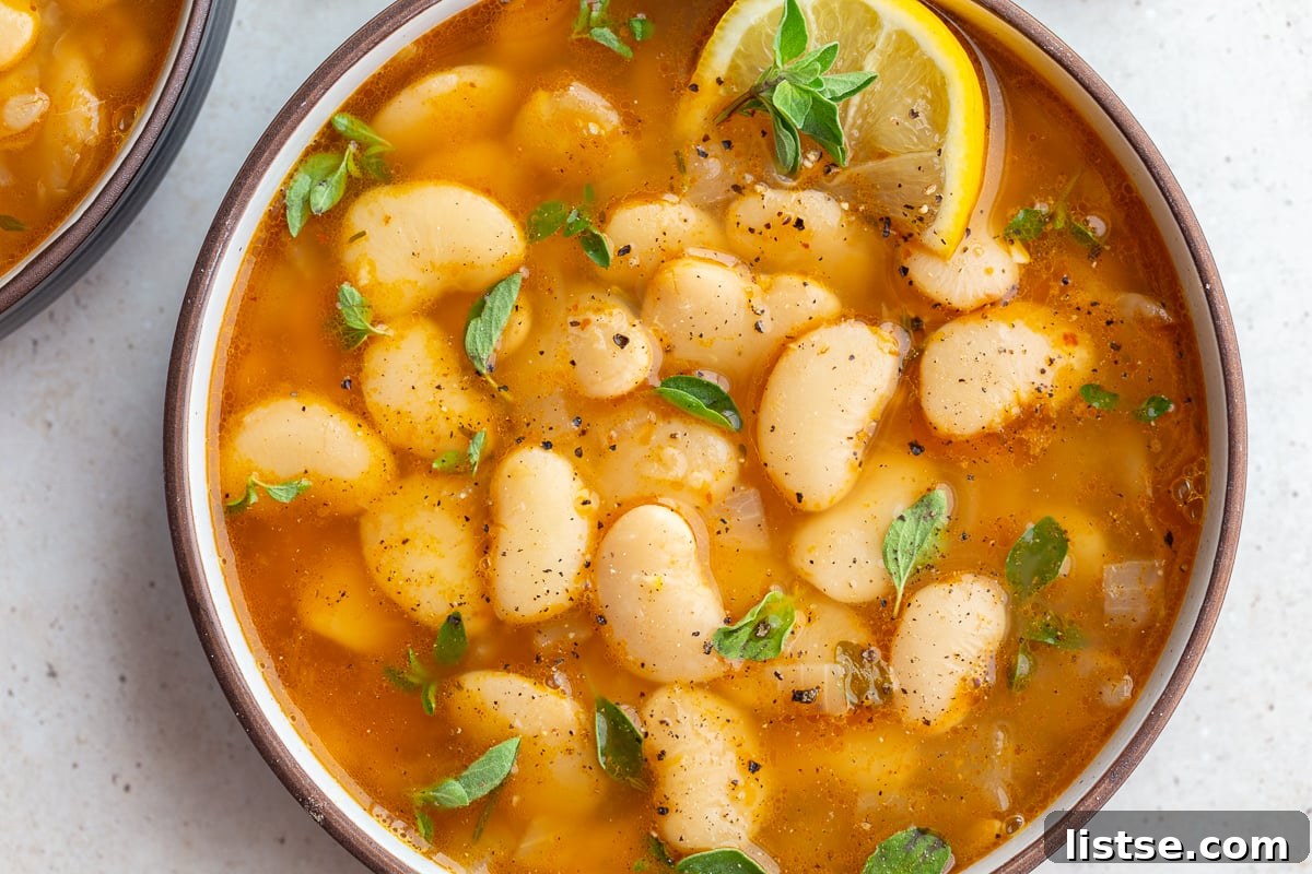 A large bowl of brothy beans, garnished with fresh lemon wedges and green herbs, highlighting the rich broth and tender beans.