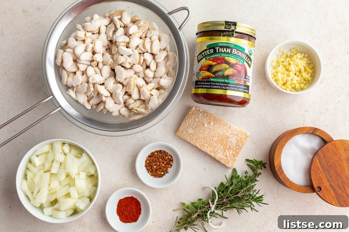Various ingredients for brothy beans laid out on a wooden surface, including dry lima beans, onions, garlic, fresh herbs, and spices.