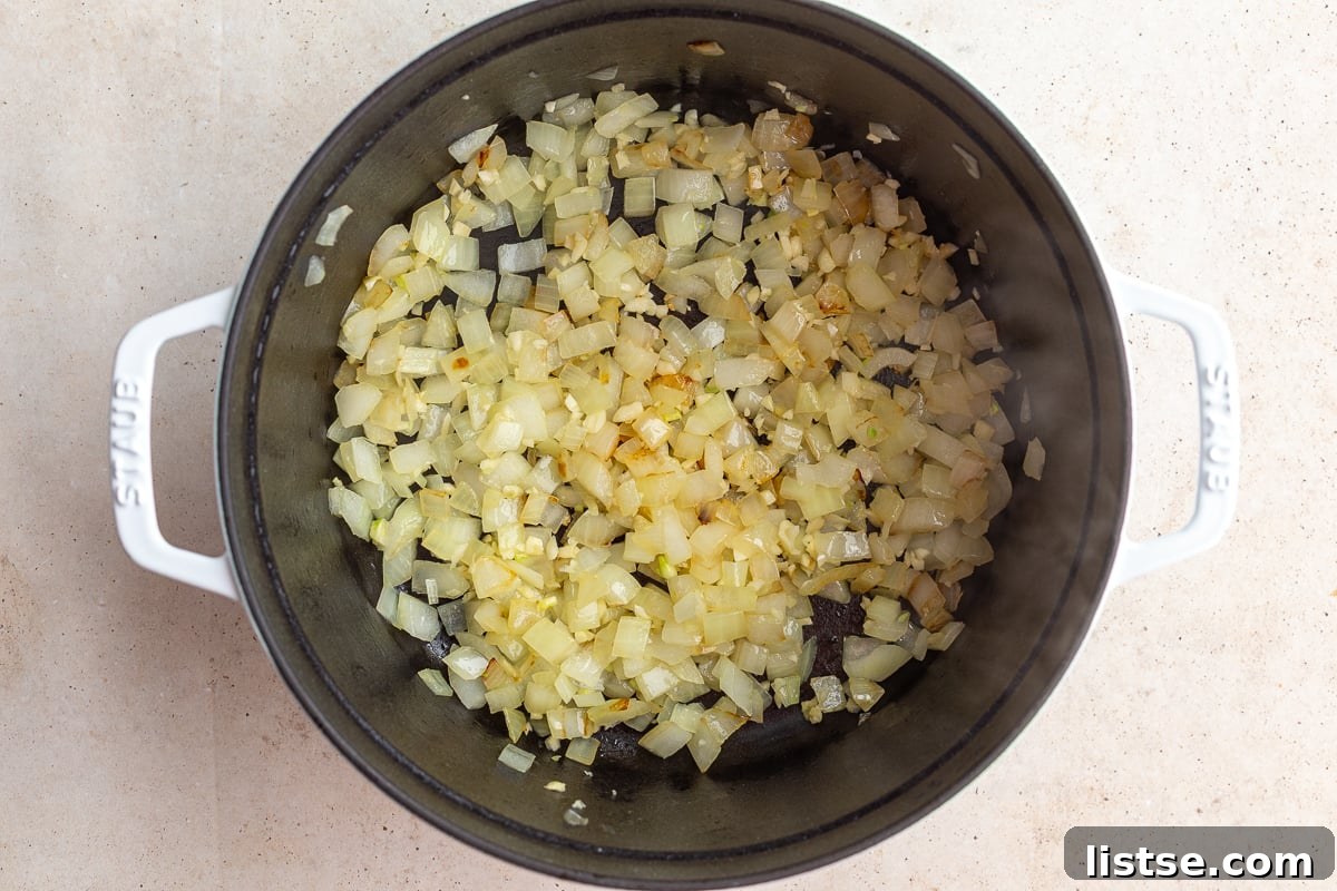 Diced yellow onions being sautéed in olive oil in a large cast iron Dutch oven over medium heat.