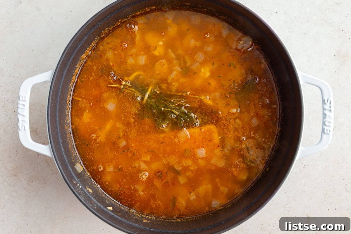 A large pot of brothy beans simmering, with the herb bundle visible on top of the rich, simmering broth.