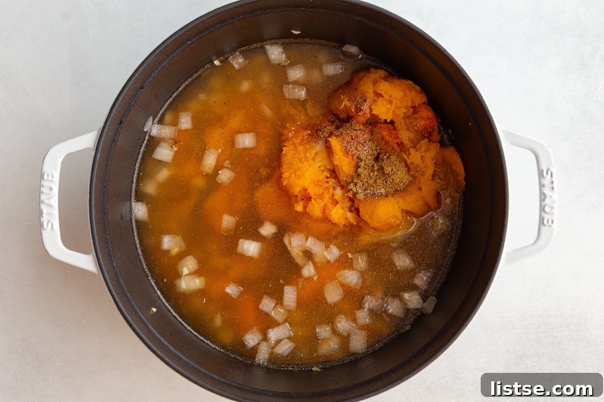 butternut squash soup in a pot before it's been blended. you can see the onions and chunks of squash floating in the pot of broth