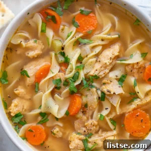 A bowl of vegetarian chicken noodle soup, garnished with fresh herbs and a lemon slice.