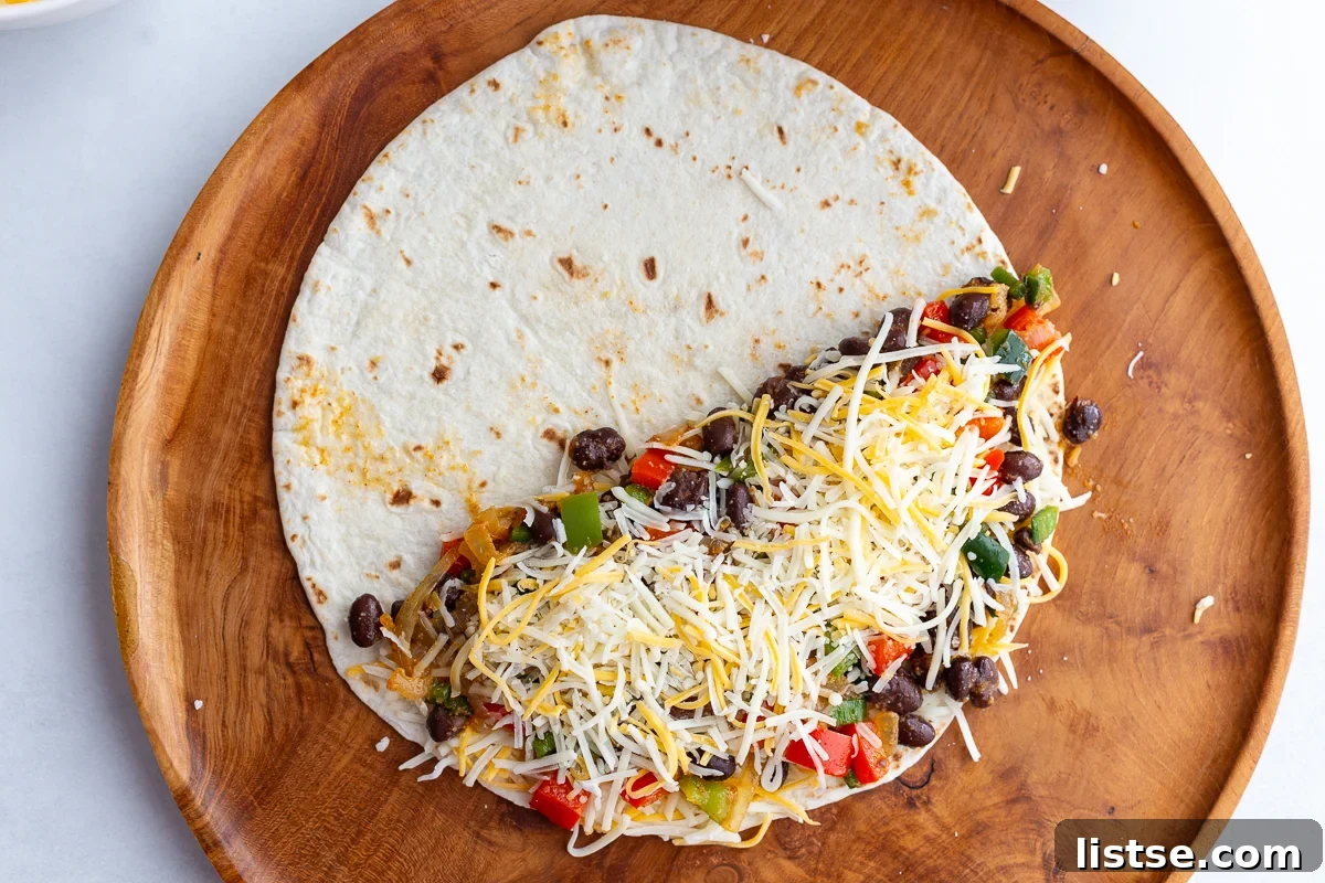 Effortless Meatless Quesadillas 7 An uncooked vegetarian quesadilla on a wooden board, showcasing the black bean and vegetable filling layered with shredded cheese.