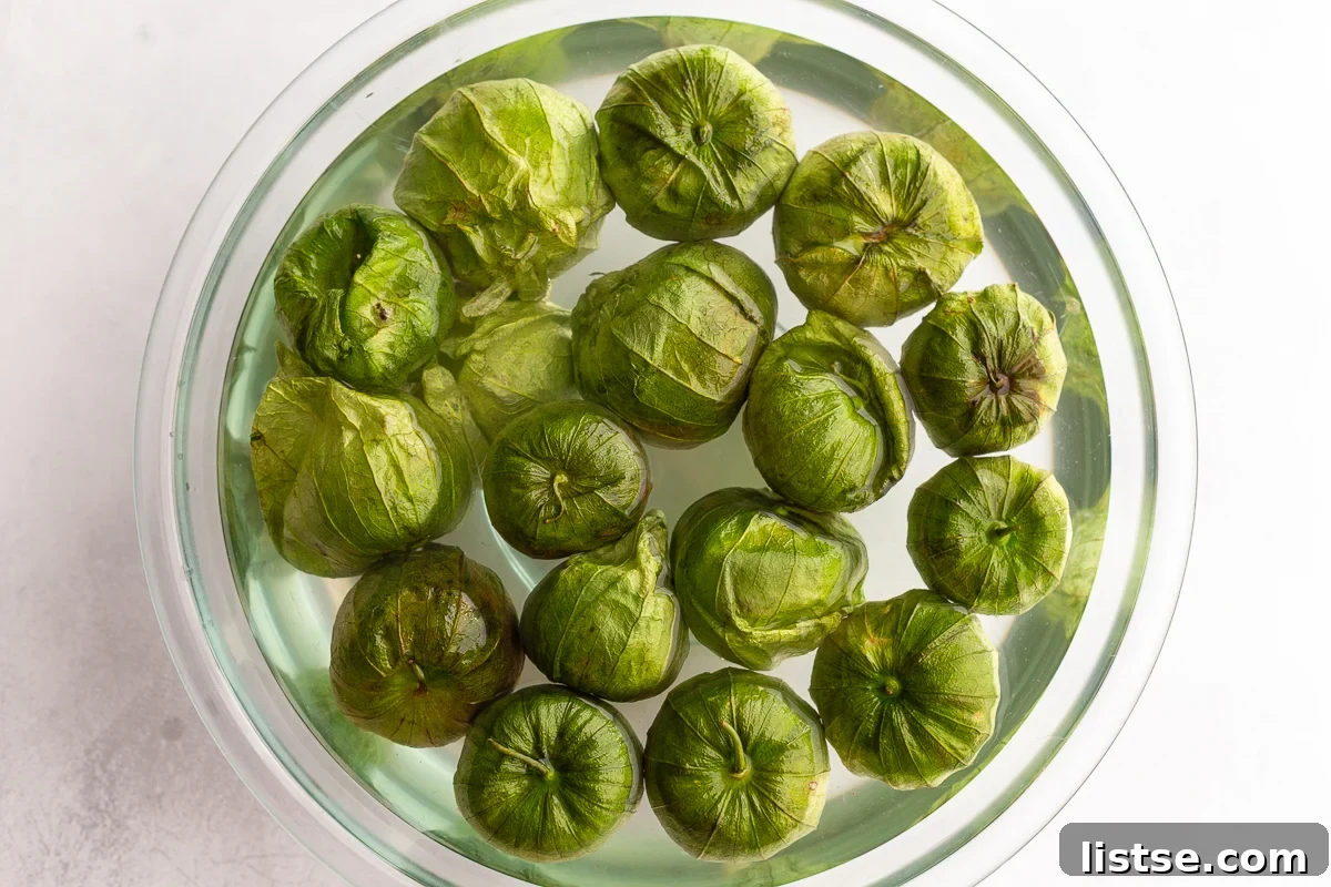 Tomatillos soaking in a bowl of water, preparing for easy husk removal.