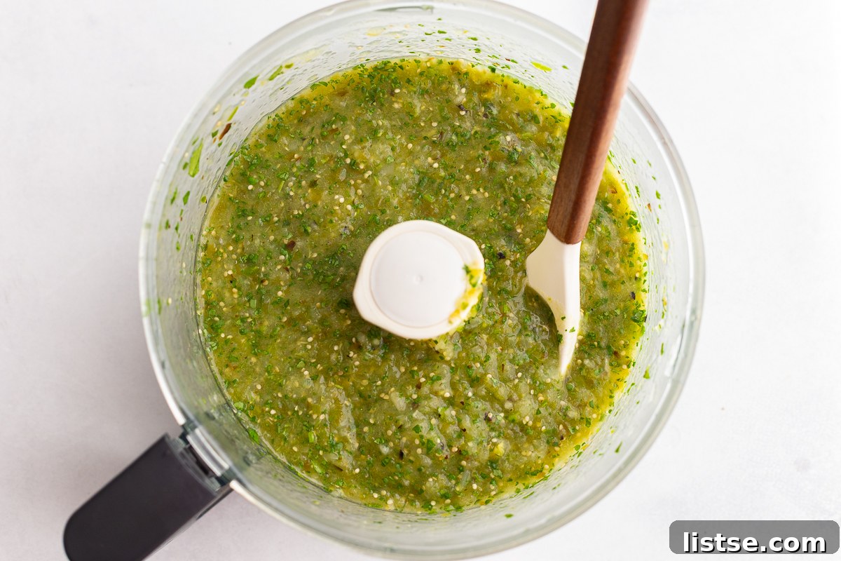 The blended tomatillo salsa in a food processor, showing a smooth yet slightly textured consistency.