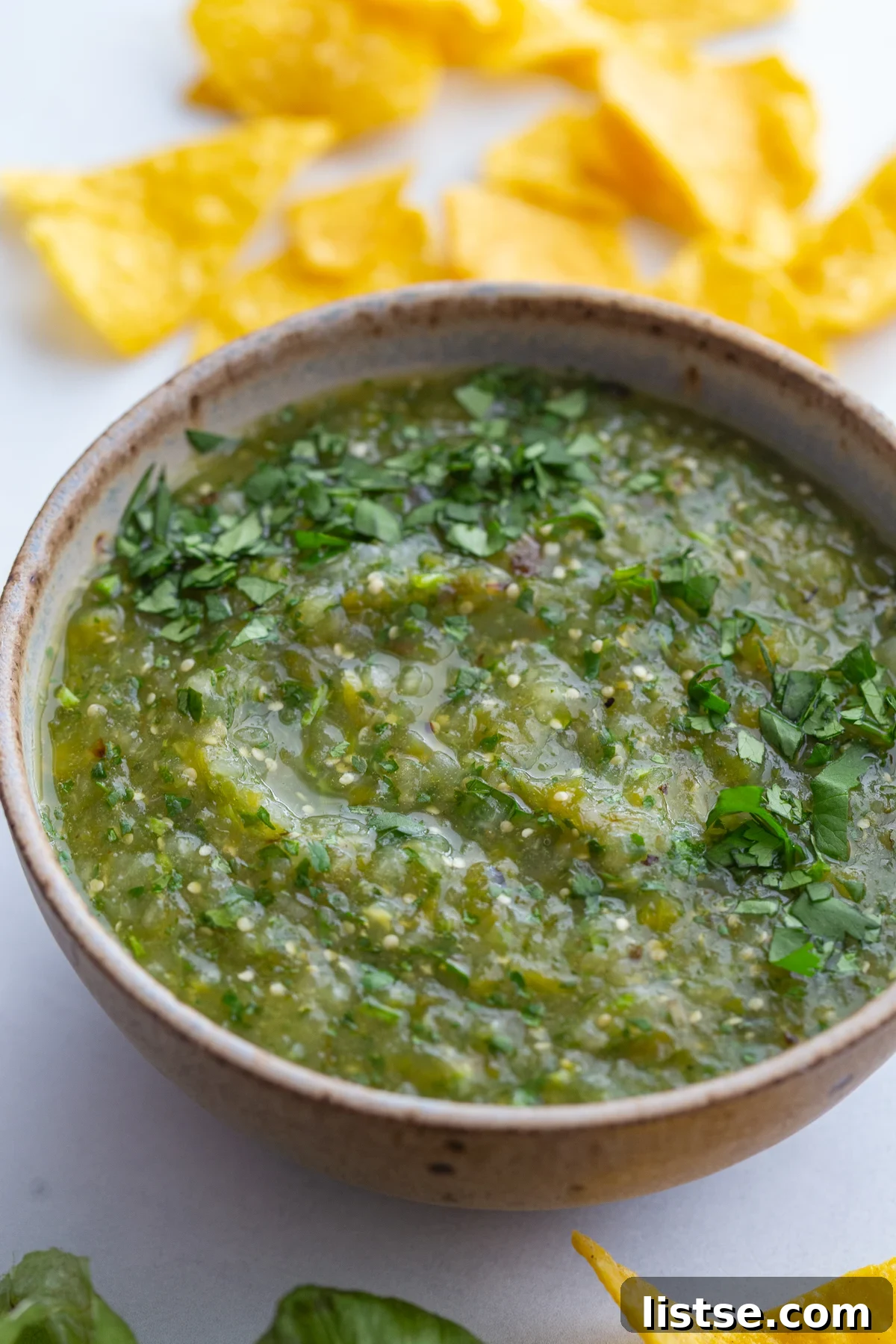 A large bowl of roasted salsa verde sits on a rustic wooden surface, garnished with fresh cilantro leaves.
