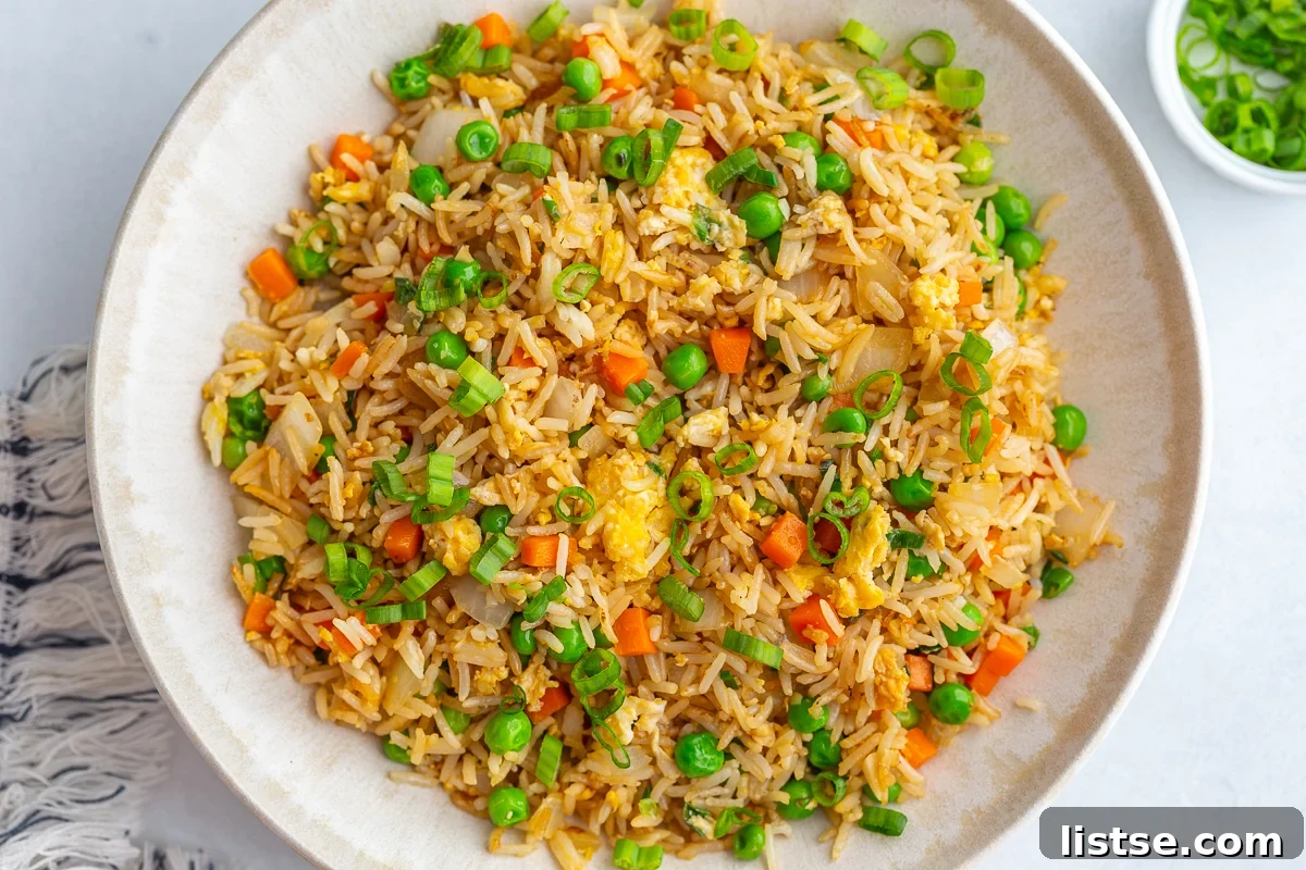 A large white bowl filled with perfectly cooked homemade vegetarian fried rice, richly garnished with fresh green onions and a sprinkle of sesame seeds, highlighting its vibrant colors and inviting texture.