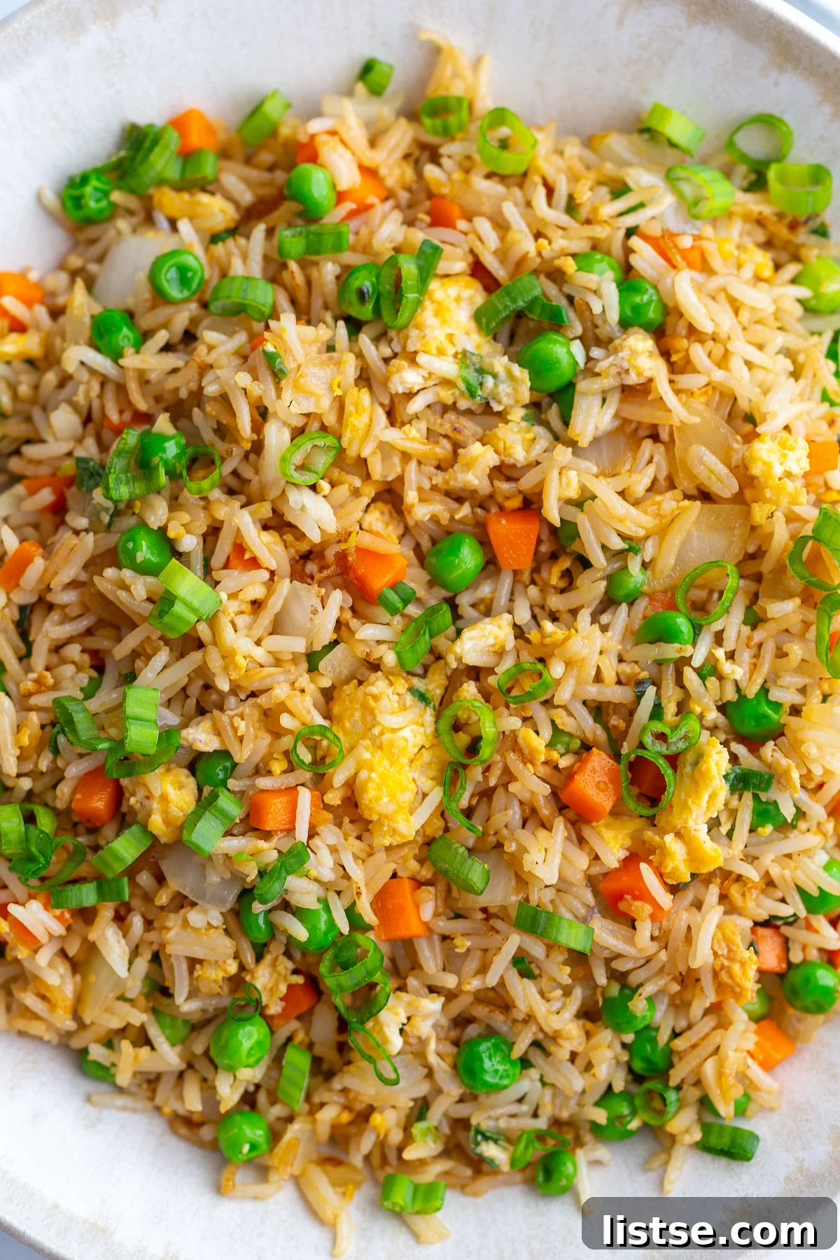 A vibrant and close-up view of the perfectly cooked vegetarian fried rice resting in a large white bowl, elegantly garnished with freshly chopped green onions, showcasing its appetizing appearance and texture.