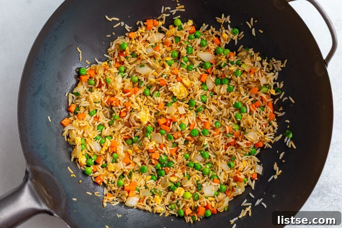 Vibrant vegetarian fried rice cooking actively in a large wok, with all ingredients mixed together, just before the final seasoning and serving, showing steam and rich colors.
