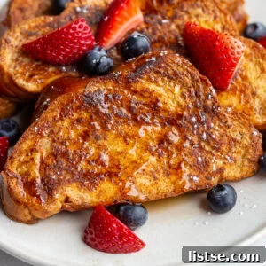 Perfectly golden French Toast slices artfully arranged on a plate, adorned with a medley of fresh strawberries and blueberries.