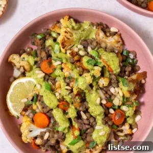 Warm lentil salad topped with green goddess dressing and a lemon wedge, served in a rustic bowl.