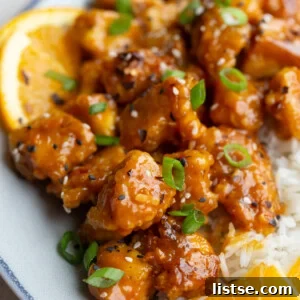 Crispy orange tofu served on a plate with fluffy rice and fresh orange slices.