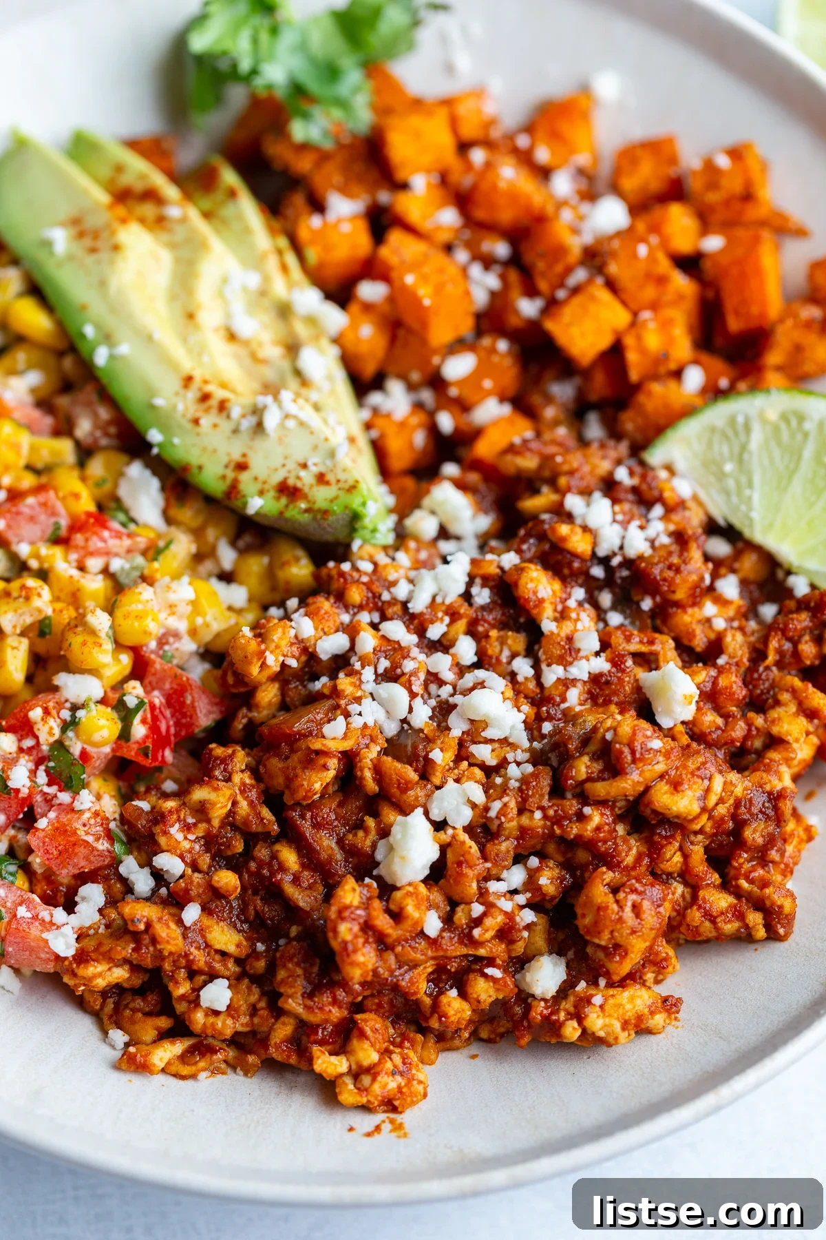 Vibrant Street Corn Tofu Bowls showcasing roasted sweet potatoes, seasoned ground tofu "meat", creamy avocado slices, a zesty lime wedge, and a fresh Mexican street corn salad in an inviting presentation.