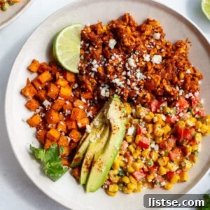 Street corn tofu bowls with roasted sweet potato, ground tofu "meat", sliced avocado, lime wedge, and street corn salad in a bowl