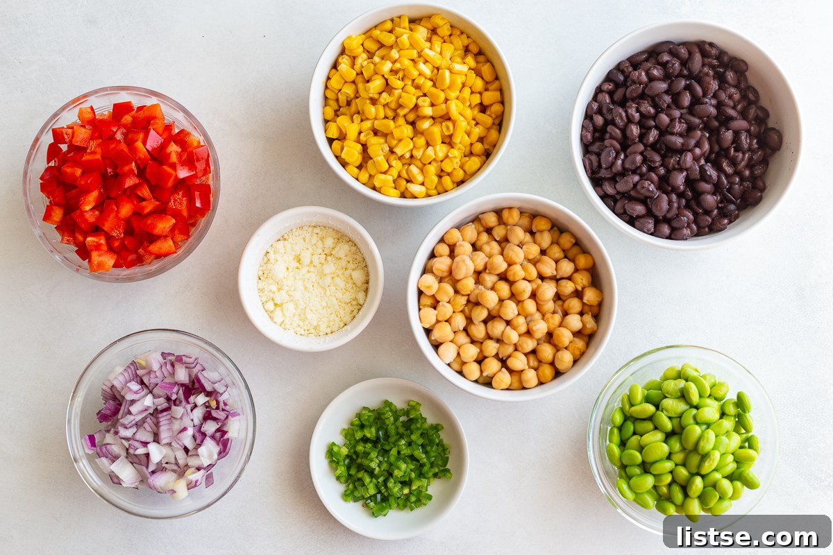 Ingredients for the street corn bean salad laid out on a surface, including canned beans, corn, edamame, bell pepper, onion, and cotija cheese.