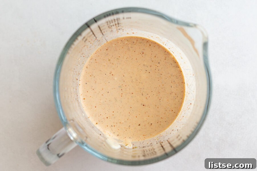 The creamy elote dressing whisked together in a glass measuring cup.