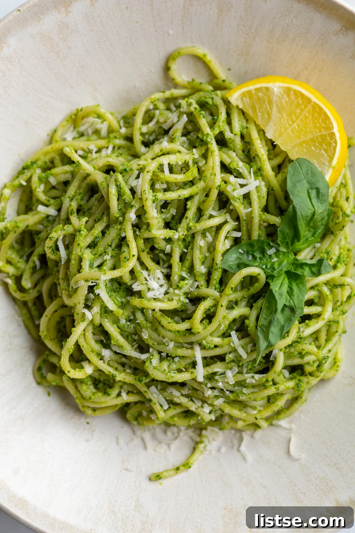 pesto pasta on a plate with a lemon wedge and fresh basil