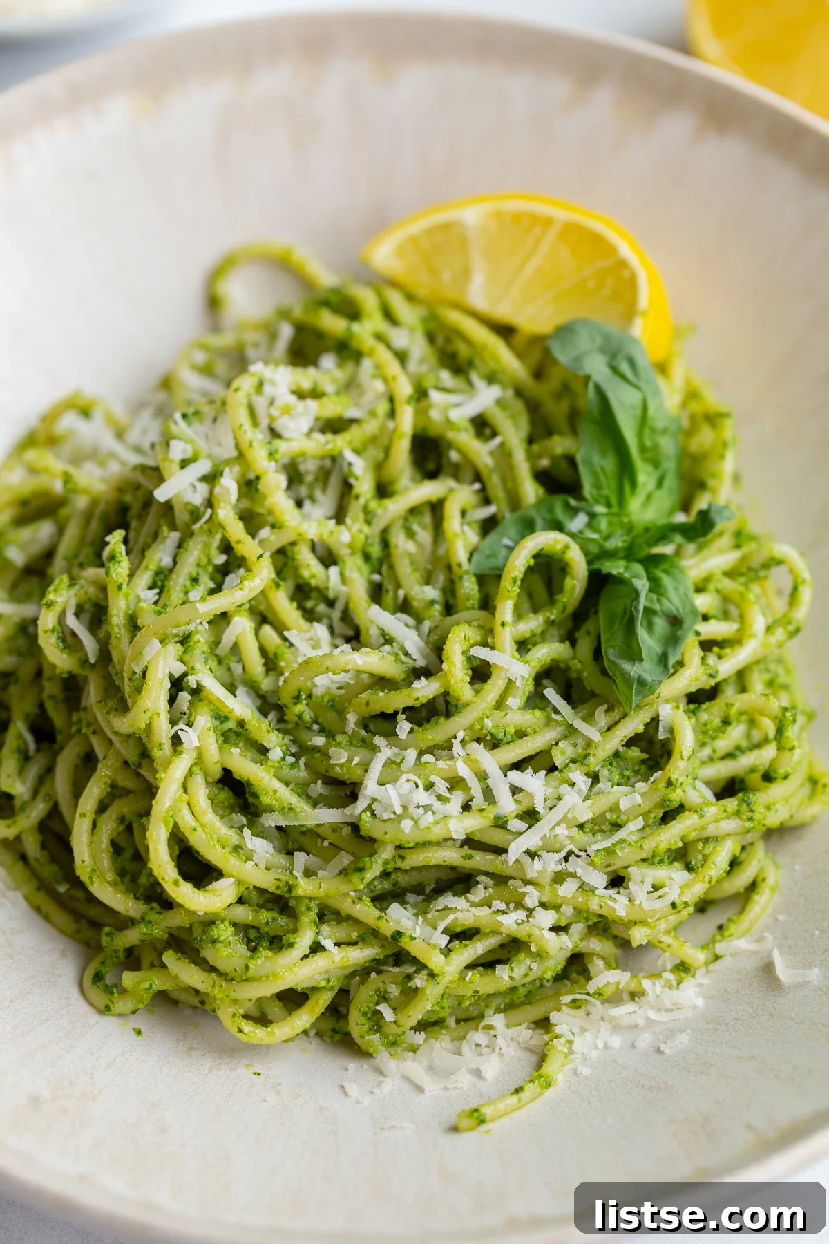 pesto pasta on a plate with a lemon wedge and fresh basil