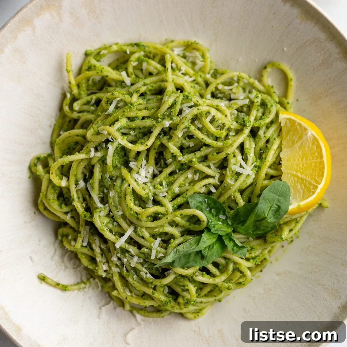pesto pasta on a plate with a lemon wedge and fresh basil