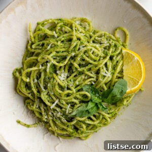 pesto pasta on a plate with a lemon wedge and fresh basil