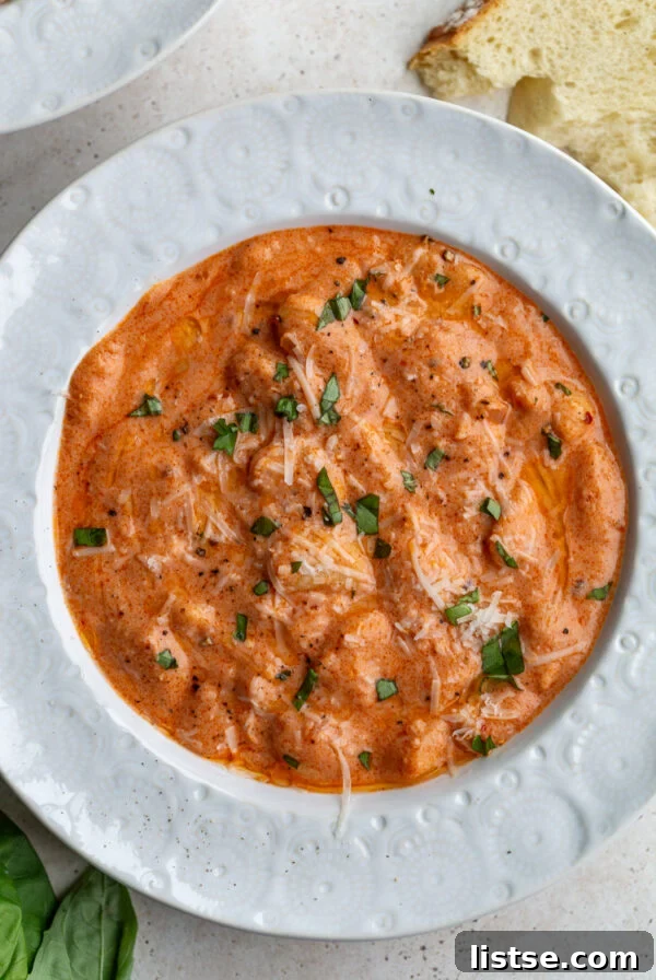 vodka sauce butter beans on a white bowl topped with basil and parmesan cheese