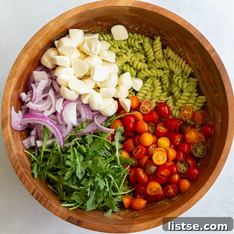 Pesto Pasta Salad with Cherry Tomatoes and Mozzarella 8 pesto pasta in a large wood bowl with mozzarella, tomatoes and arugula on top before being mixed in