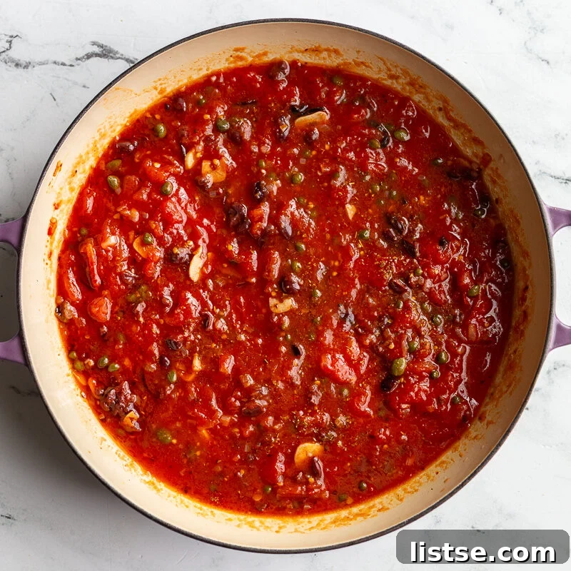 Classic Pasta Puttanesca Recipe with Anchovies and Olives 7 Puttanesca tomato sauce simmering in a skillet with olives and capers.