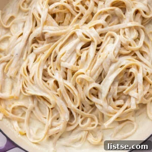 White creamy sauce tossed with pasta in a pot.