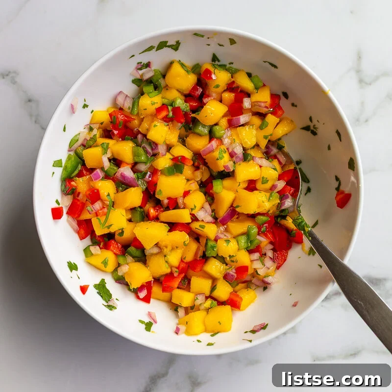 Cilantro-Lime Tofu with Fresh Mango Salsa 7 Overhead shot of mango salsa with diced mango, red bell pepper, red onion, and cilantro in a white bowl with a spoon.
