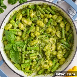 pesto gnocchi in a large skillet with fresh basil and lemon in the corners of the shot