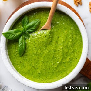 Homemade Walnut Pesto Recipe 11 Walnut pesto in a white bowl on a wooden board with a wooden spoon resting inside, surrounded by fresh basil, lemons, and walnuts